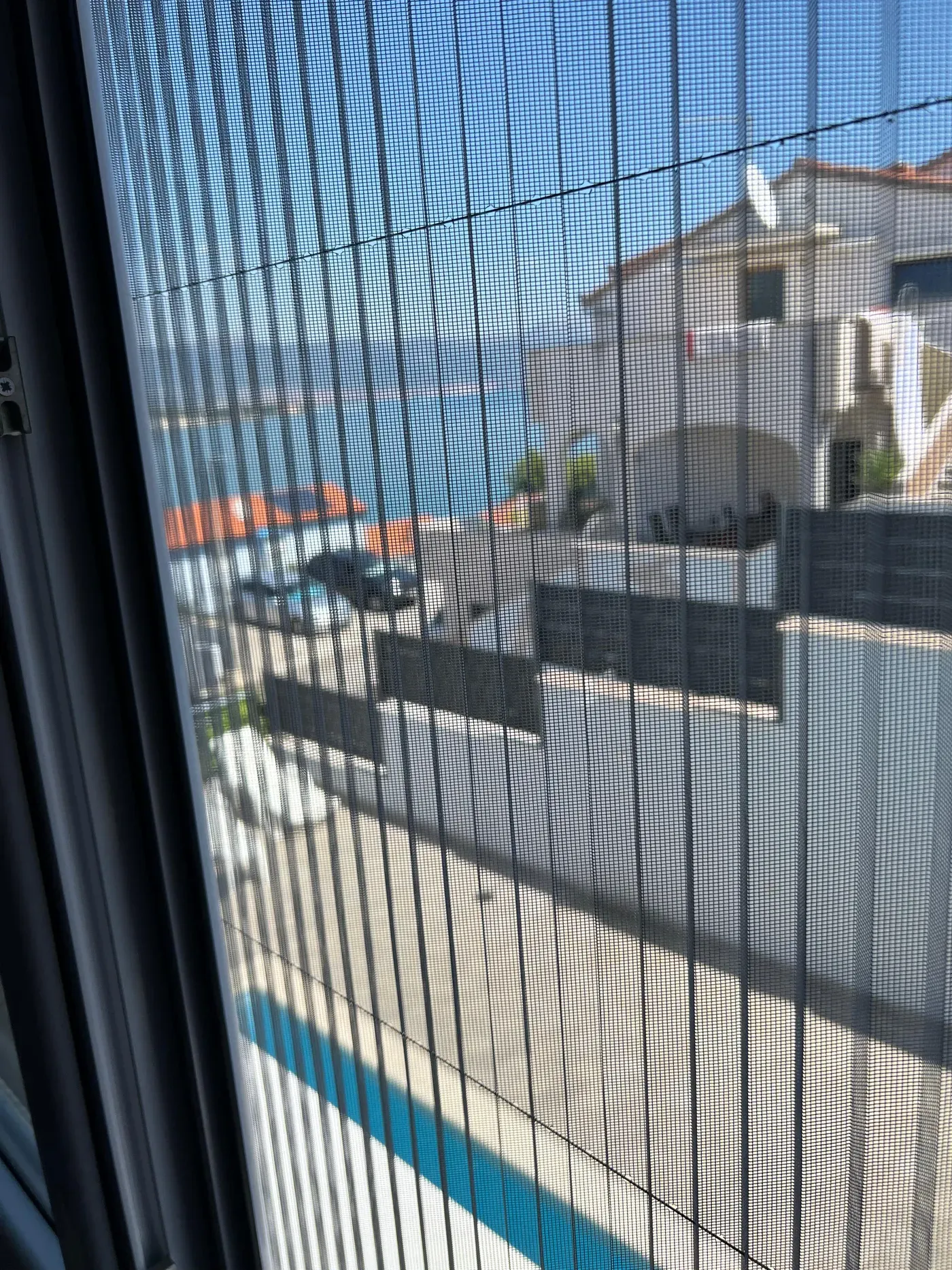 Detalj nabrane plise mreže, iza nje kuće i more